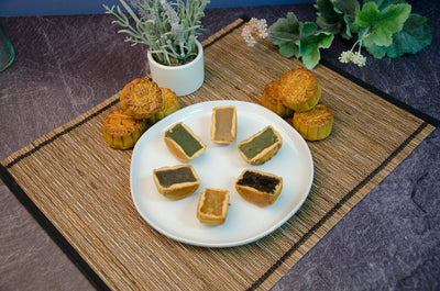 Mini Tea & Chestnut, Longan, Oolong, Green Tea, Jasmine, Pomelo Mooncakes cut to see filling, all on a white plate.