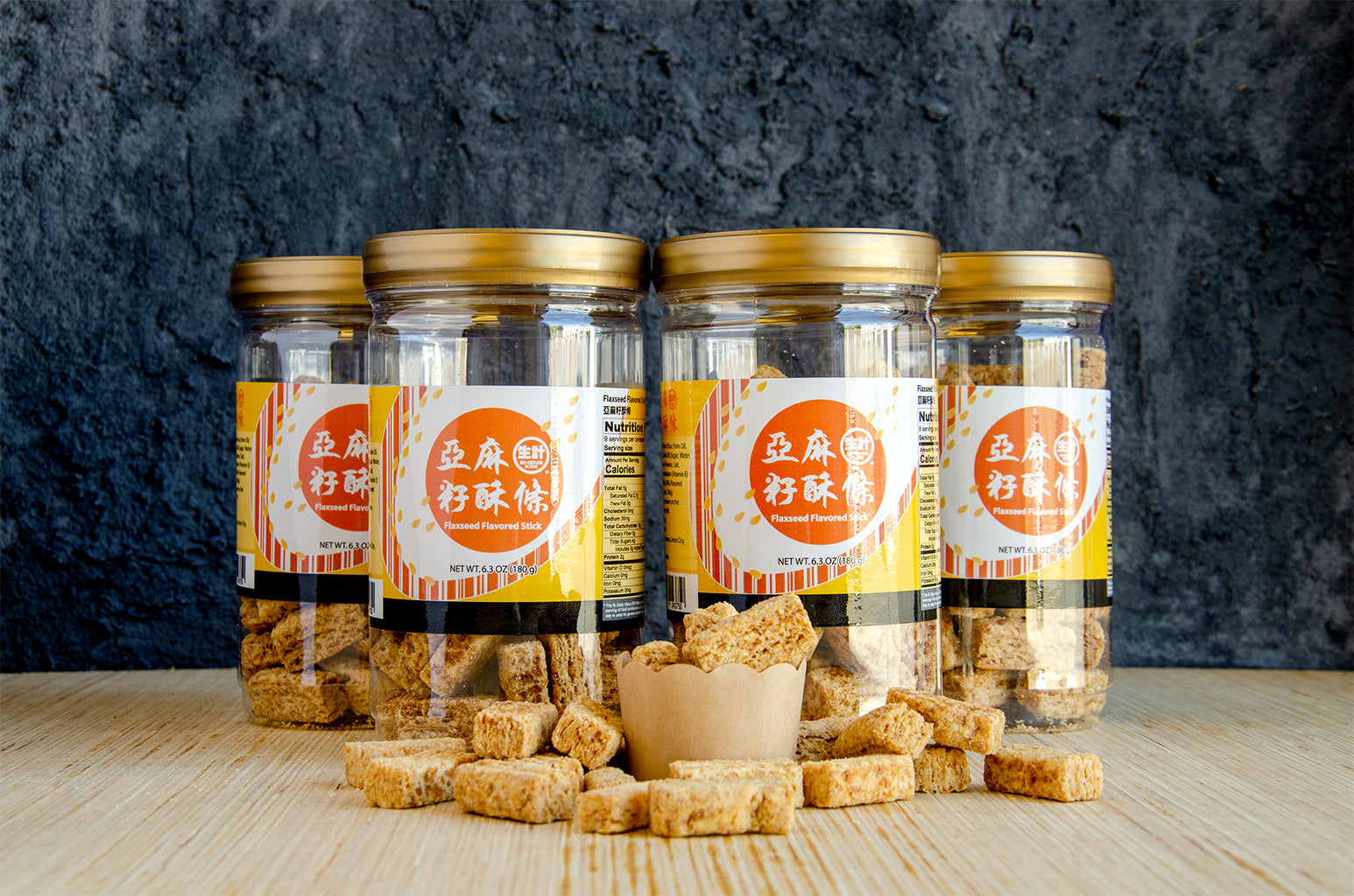 4 jars of Flakey Flaxseed Biscuits. One small cup of Flakey Flaxseed Biscuits in front of closed jars. Some Flakey Flaxseed Biscuits spilled in front of the jars and small cup.
