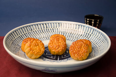 Mini Date, Lotus, Red Bean Mooncakes on blue and white dish on red table cloth with a decorative black cup behind.