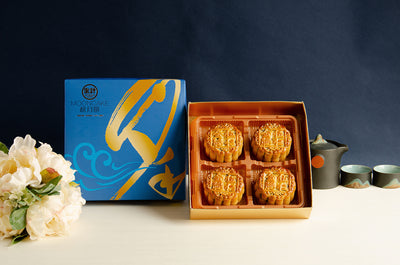 A set of four golden-brown mooncakes with a mix of nuts and ham, presented in a box with a floral design.