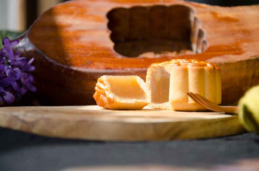 Small Lotus Mooncake cut to see filling on a wooden board with a traditional mooncake press behind.