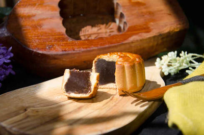 Small Red Bean Mooncake cut to see filling on wooden board with a traditional mooncake press behind.